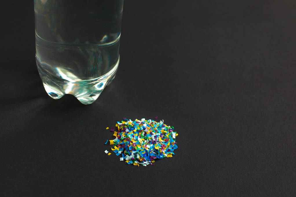 Microplastic contaminated water in the bottle. A pile of microplastic that is taken out of the water on a black background. Dangerous additives. Toxic substances.