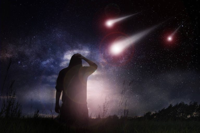 A science fiction edit of a man standing in a field as meteorites speed towards the earth at night with the stars in the sky